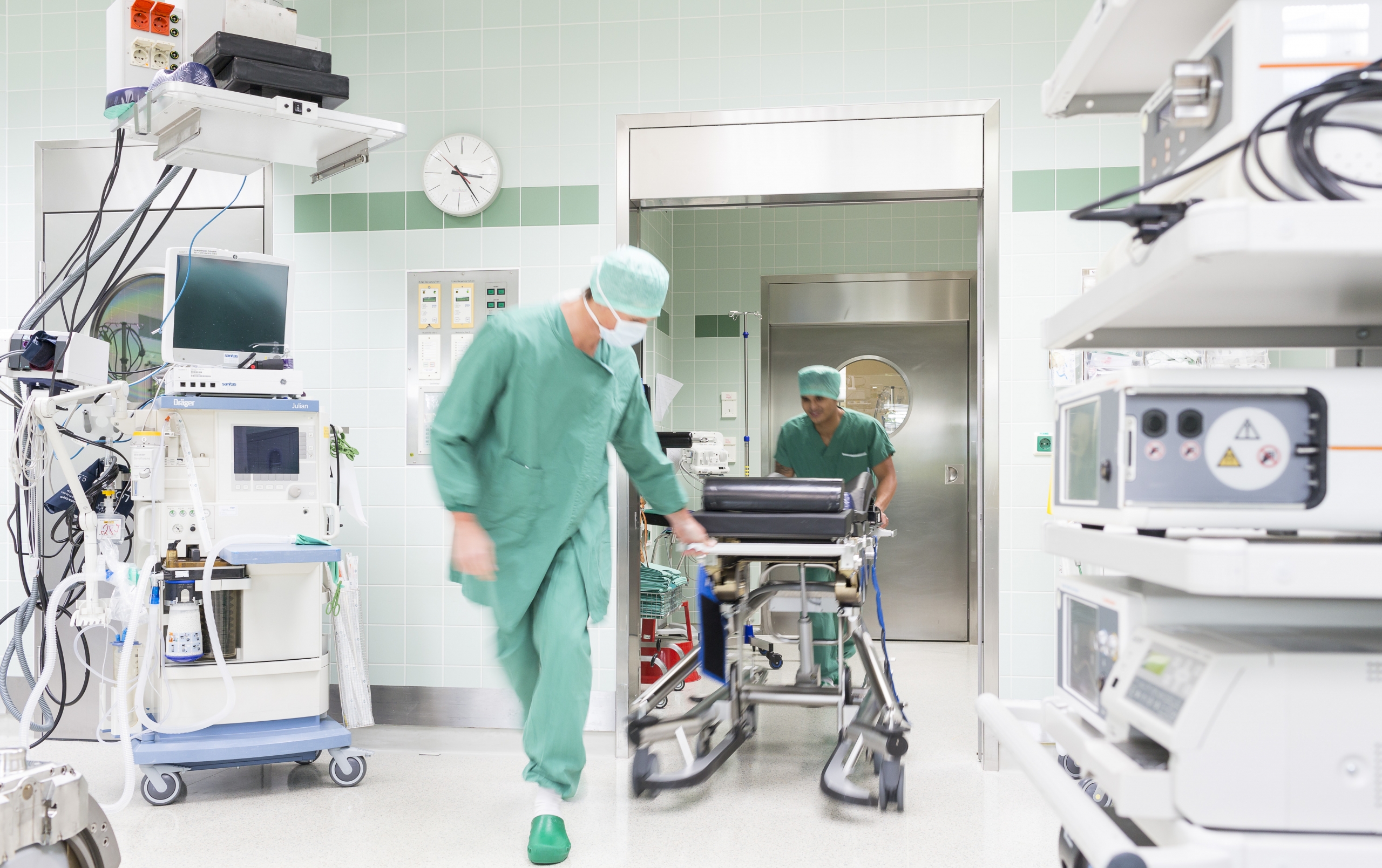Zwei Klinik-Mitarbeiter schieben eine Kranken-Bahre in den OP